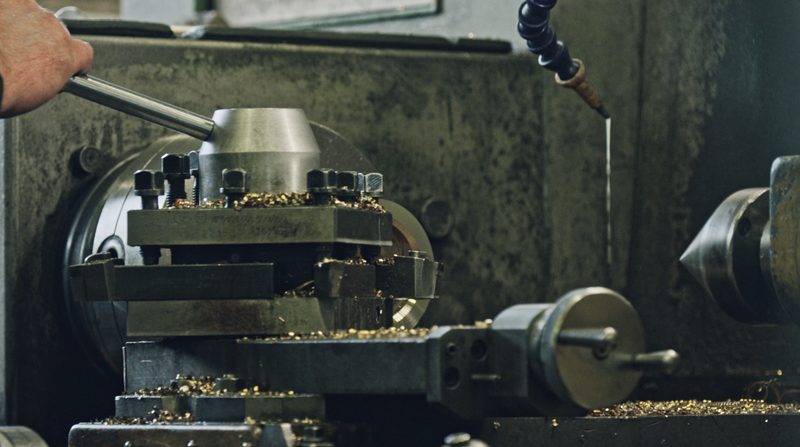 Hand am Hebel einer Drehmaschine, auf dem Support liegen frische Metallspäne
