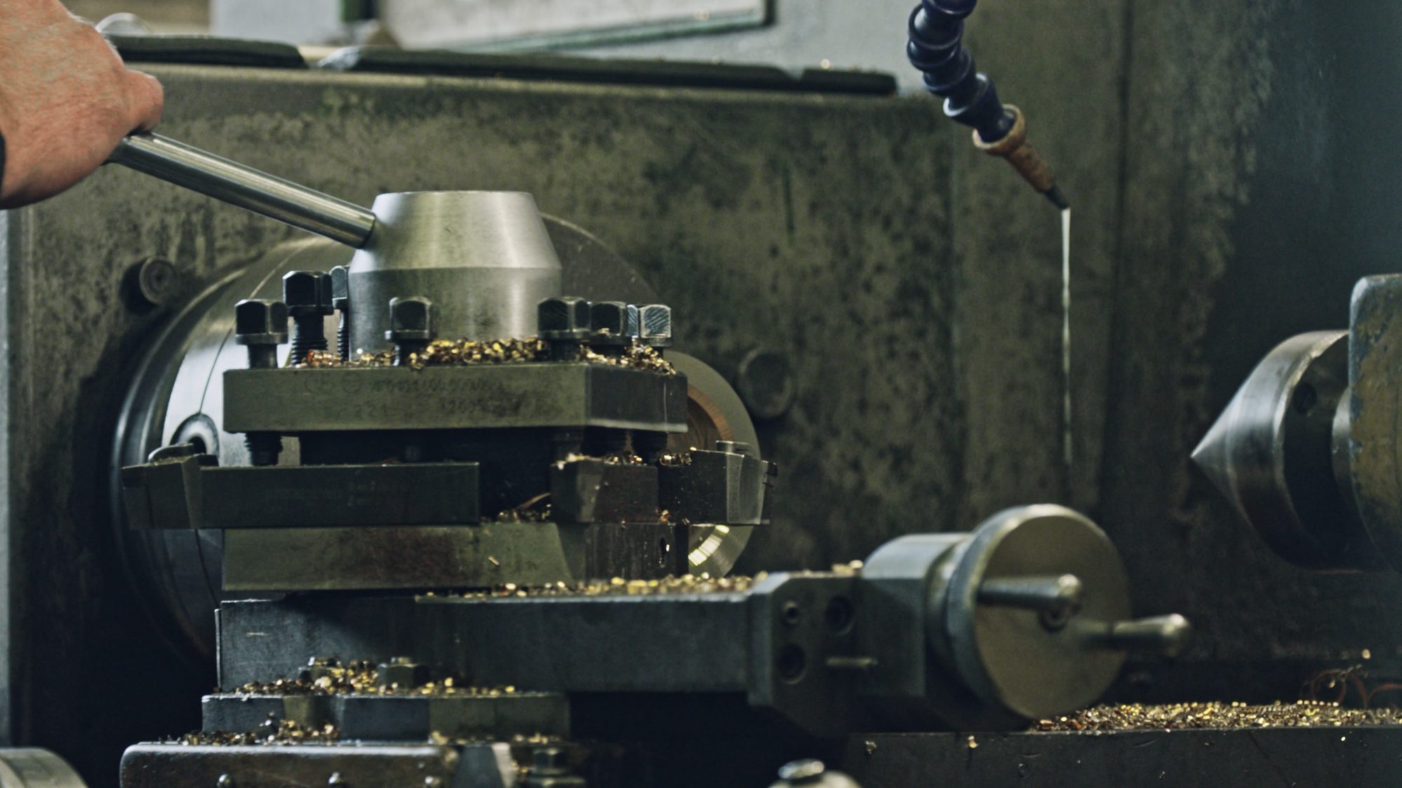 Hand am Hebel einer Drehmaschine, auf dem Support liegen frische Metallspäne